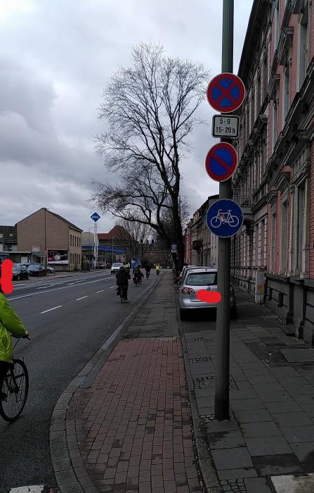 Dooringradweg in Duisburg mit KFZ rechts vom Radweg und Radfahrenden auf der Fahrbahn. Ein Schild weist auf die Nutzungspflicht des Radweges hin.