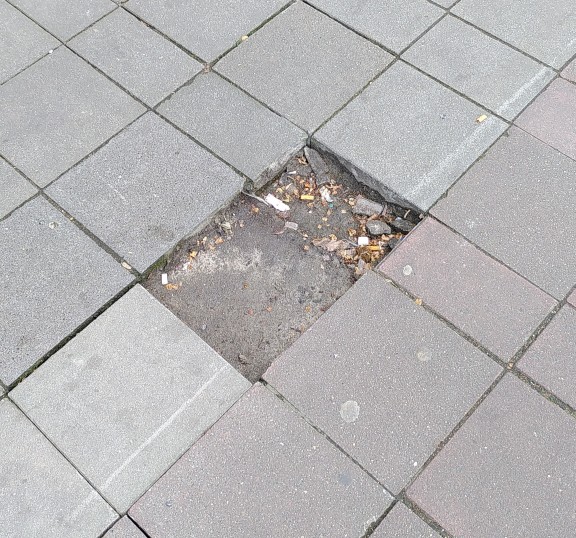 Zwei Gehwegplatten fehlen und wurde extrem schlecht notdürftig geflickt mit deutlich Stolperkante