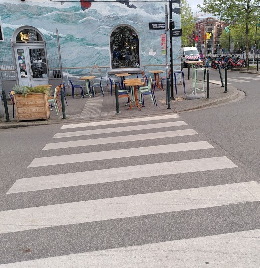 Zebrastreifen und ein Gehweg der stark mit Tischen zugestellt ist. Inkl. Teile des Bereichs des Zebrastreifens