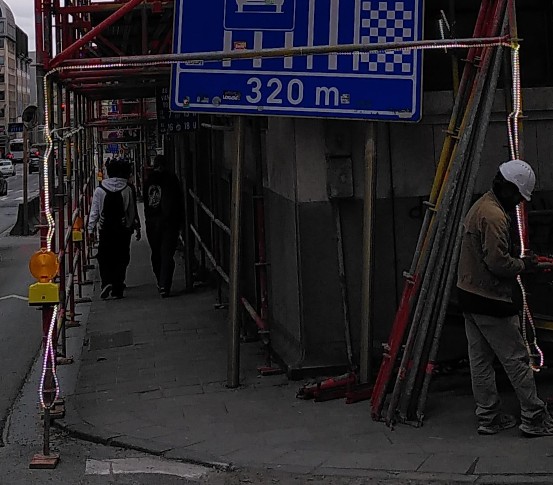 Ein Gerüst überspannt den Gehweg und ein Arbeiter befestigt gerade eine LED-Lichtschlange