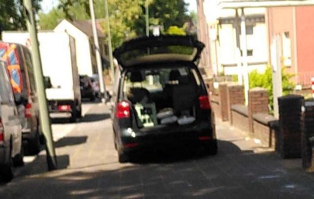 KFZ steht mitten auf dem Gehweg und blockierten diesen erheblich. Ein paar Meter weiter sind legale freie Parkplätze am Fahrbahnrand. Der Kofferraum ist zum entladen geöffnet.