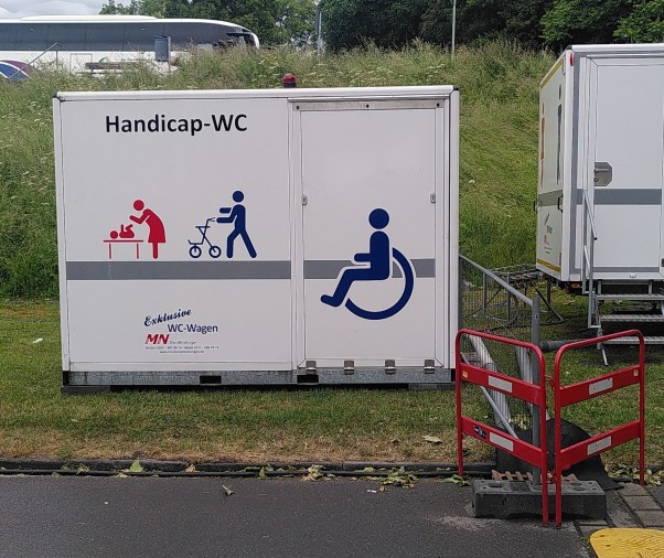 Container mit Handi-Cap WC, darauf abgebildet Rollstuhlsymbol, Rollatorsymbol und Symbol für Wickeln von Kindern