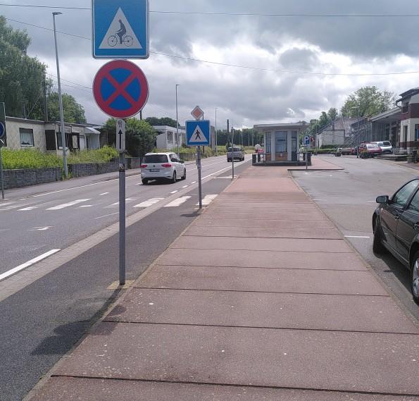 Das Bild zeigt zwei Verkehrseichen, im Hintergrund das blaue Schild mit weißem Dreieck und schwarzem Fußgänger ähnlich dem deutschen für Zebrastreifen im Vordergrund eine blaues Schild mit weißem Dreieck und einem symbolisierten Fahrrad mit Fahrer.