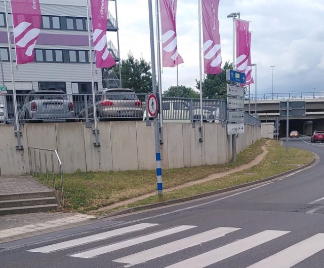 Ein Fußverkehr Verbotsschild vor einem Trampelpfad durch eine Fläche mit Rasen, der offensichtlich häufig benutzt wird.