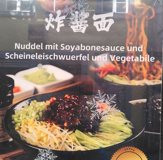 Die Abbildung zeigt ein Gericht, asiatische Schriftzeichen und den Text: "Nuddel mit Soyabonesauce und Scheineleischwuerfel und Vegetabile"