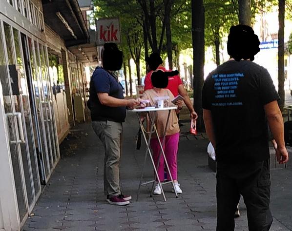 Stehtisch mit einem Mann und einer Frau, wohl von der SPD. Stehen auf einem schmalen begehbaren Streifen und blockieren diesen weitestgehend.