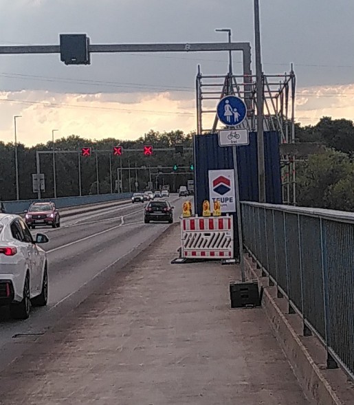 Ein schmaler Rad-Gehweg wird durch eine Baustelle verengt und aus dem Mischweg wird durch ein Schild ein Gehweg mit Fahrrad Frei.