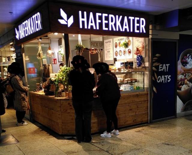 Köln HBF, Ladenlokal von Haferkater mit Kundschaft und Firmenschild.