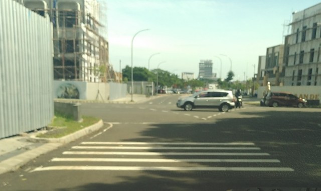 Sicht vom Beifahrersitz eines KFZ auf eine Kreuzung. Vor dem Fahrzeug sind mehrere weiße Linien, die leichte Erhebungen darstellen.