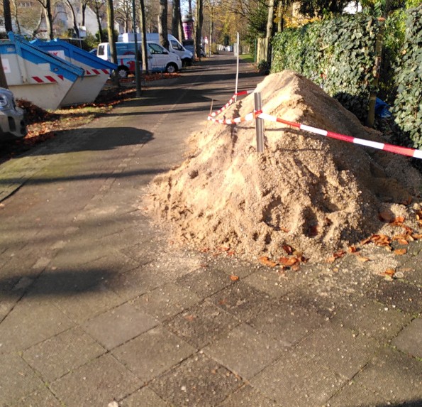 Gehweg in Düsseldorf durch großen Sandhaufen auf wenige Zentimeter verengt