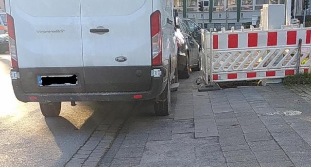 Weißer Transporter steht an Engstelle neben Baustelle auf Gehweg.
