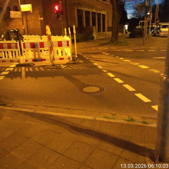 Eine Baustellenabsperrung mit einem Bagger links neben der Ampel und Absperrung fast über die gesamte Breite des Ampelbereichs für Fußverkehr.