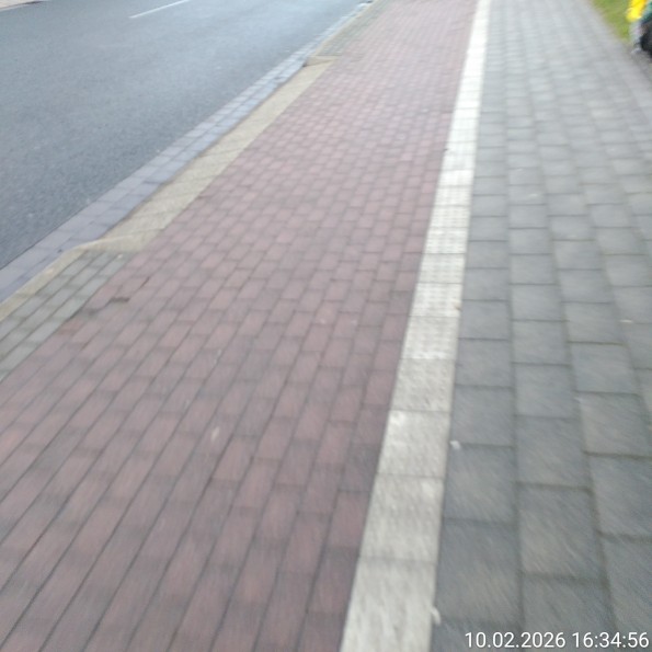Angeschrägte breite Bordsteinkante neben einem Radweg ohne Absenkung.