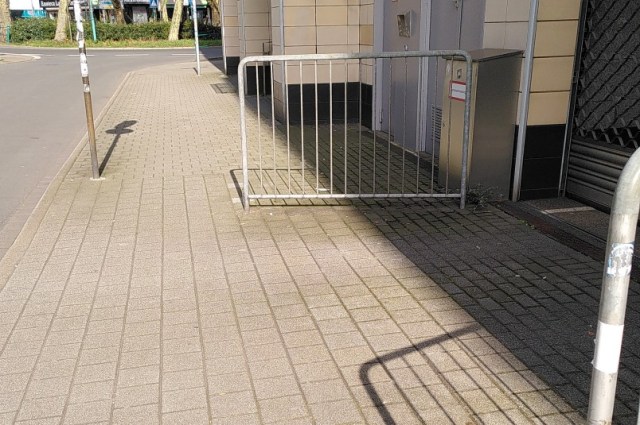 Eigentlich breiter Gehweg wird durch ein Gitter an einer Ausfahrt stark eingeengt.