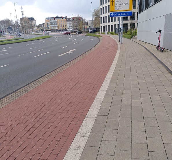 Von Rechts nach Links ein Gehweg, ein Radweg mit rotem Pflaster und vier Fahrspuren für KFZ in Duisburg
