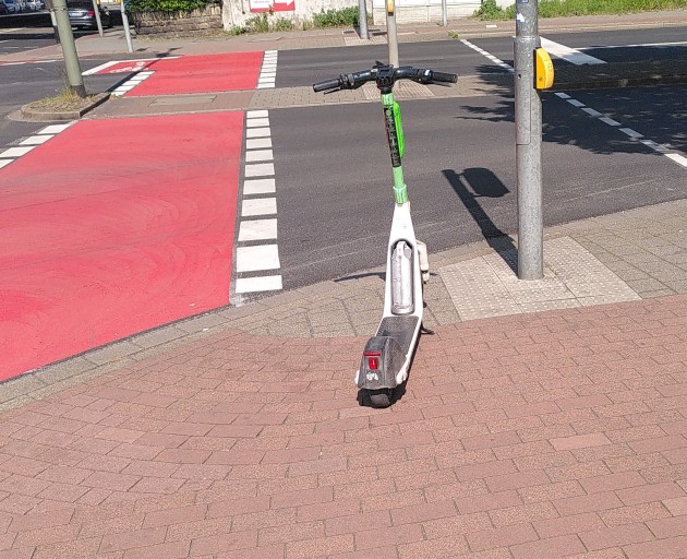 Lime Ihscooteri n Duisburg an Ampel blockiert Radweg, Gehweg und Leitlinien für Menschen mit Seheinschränkung und das Kennzeichen ist fast vollständig ab.