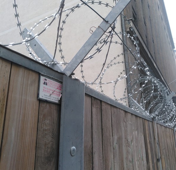 Stacheldraht in Berlin direkt am Gehweg auf Bauzaun in Kopfhöhe