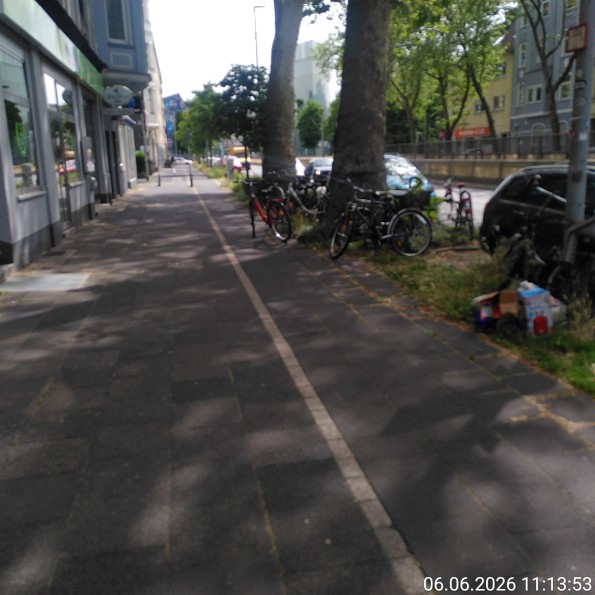 Breiter Gehweg, rechts daneben mittlerer Radweg und Parkstreifen. Auf und neben dem Radweg diverse geparkte Fahrräder