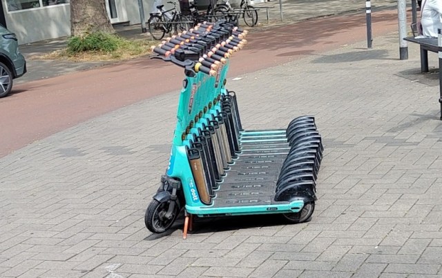 Mehrere ordentlich dicht nebeneinander aufgestellte Ihscooter auf dem "Gehweg" in einem als Spielstraße gekennzeichneten Bereich.