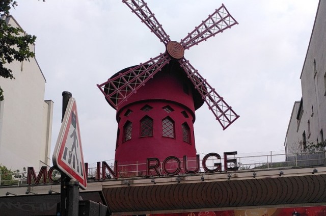 Im Vordergrund ein Verkehrsschild im Hintergrund die rote Mühle von Moulin Rouge