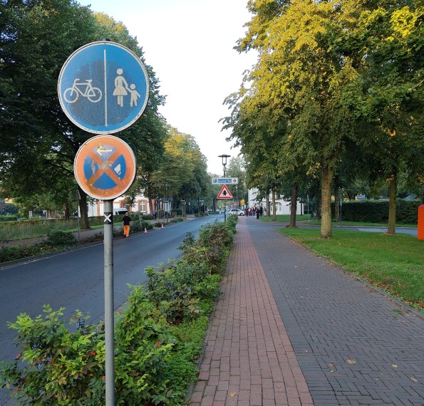 Verkehrszeichen rechts Radweg, links Gehweg, rechts neben dem Schild 1 m rotgepflastert daneben breiter anderes Pflaster.