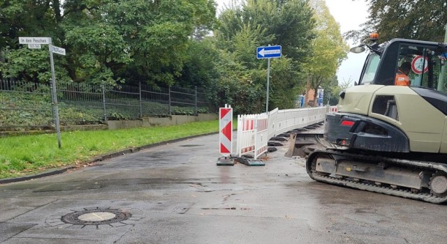Baustellenabsperrung mit Baumaschine im Vordergrund und durch das Fenster sichtbar ein Verbot für Rad- und Fußverkehr daneben eine Einbahnstraße und ein Grünstreifen