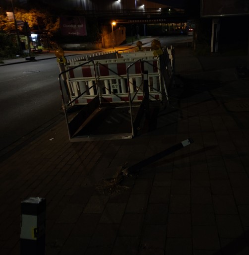 Baustellenabsperrung ohne Beleuchtung auf einem Radweg mit einer Brücke davor im Dunkeln